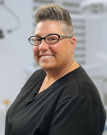 Dental hygienist wearing glasses and smiling in a dental office