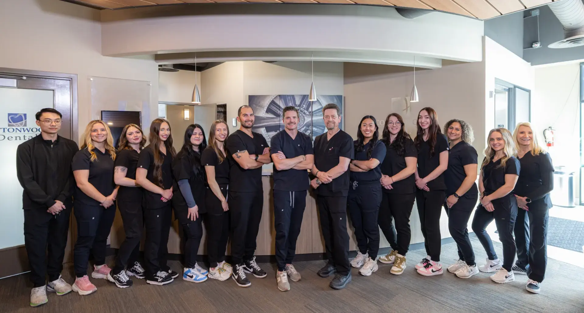 Dental team of 17 professionals in black scrubs posing together in modern Salt Lake City practice.