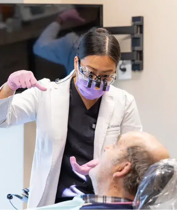 Dentist in protective gear examining patient's teeth during preventative dental care visit.